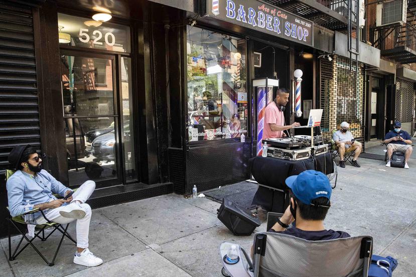 Varios clientes aguardan en la acera para que les corten el cabello mientras un DJ toca fuera de la barbería Ace of Cuts en Nueva York. (AP)