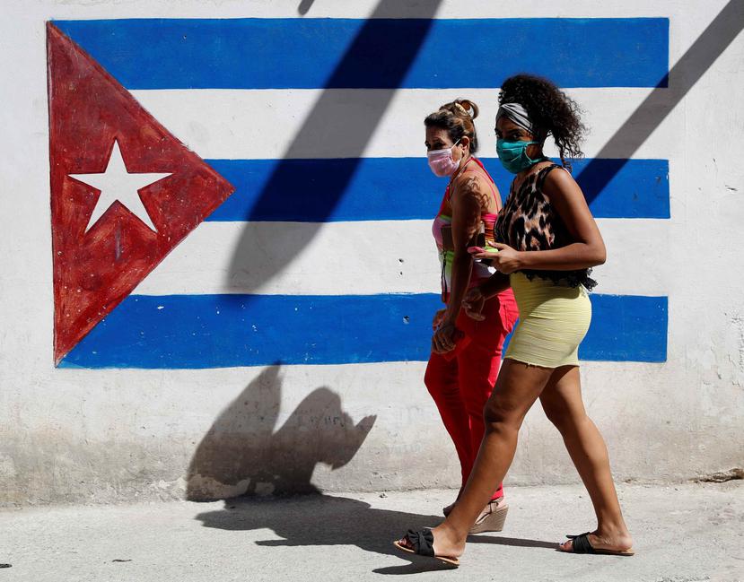 Dos mujeres caminan frente a un graffiti de la bandera cubana. (EFE)