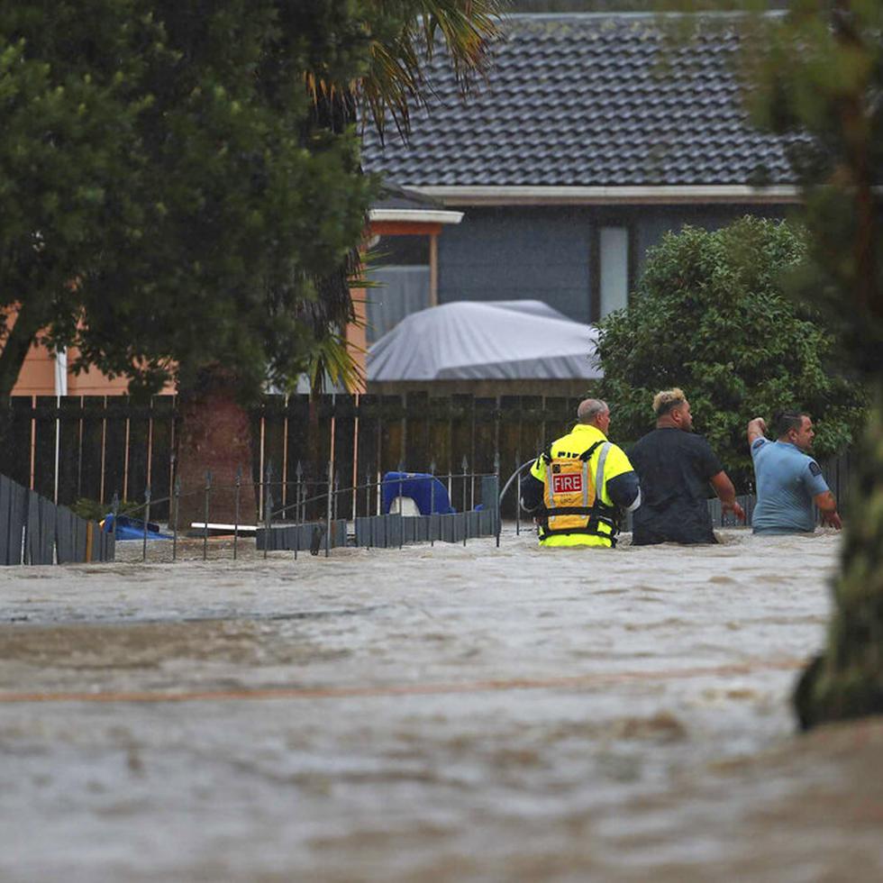Personal de emergencia y un hombre atraviesan las aguas de una inundación en Auckland, Nueva Zelanda.