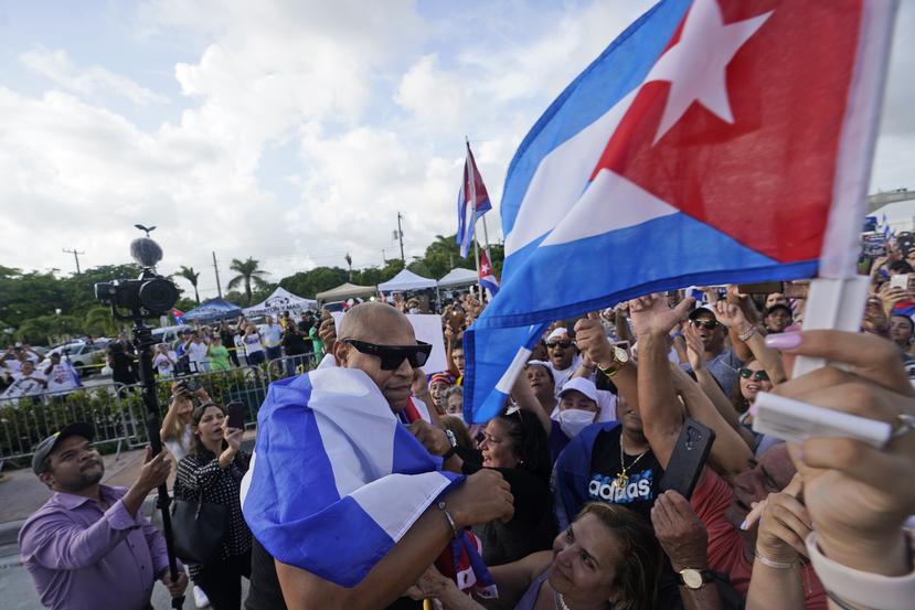Envuelto en una bandera de Cuba, el músico cubano Alexander Delgado, del dúo Gente de Zona, saluda a la multitud durante una manifestación en apoyo al pueblo cubano en el barrio de la Pequeña Habana en Miami. (AP Foto/Wilfredo Lee)