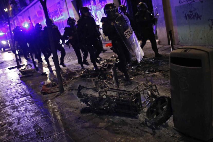 La fuerza de choque de la policía de madrid pasa cerca de una motora quemada en en el vecindario de Lavapiés. (AP)