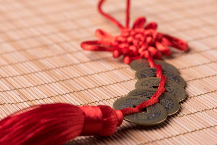 Cinco monedas chinas entrelazadas con un cordón rojo.