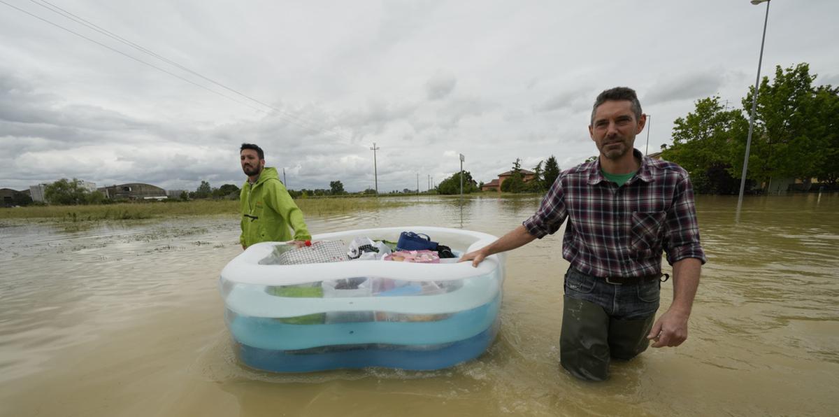 Dos hombres usan una alberca inflable para transportar sus pertenencias en un camino inundado de Lugo, Italia, el jueves 18 de mayo de 2023. (AP Foto/Luca Bruno)