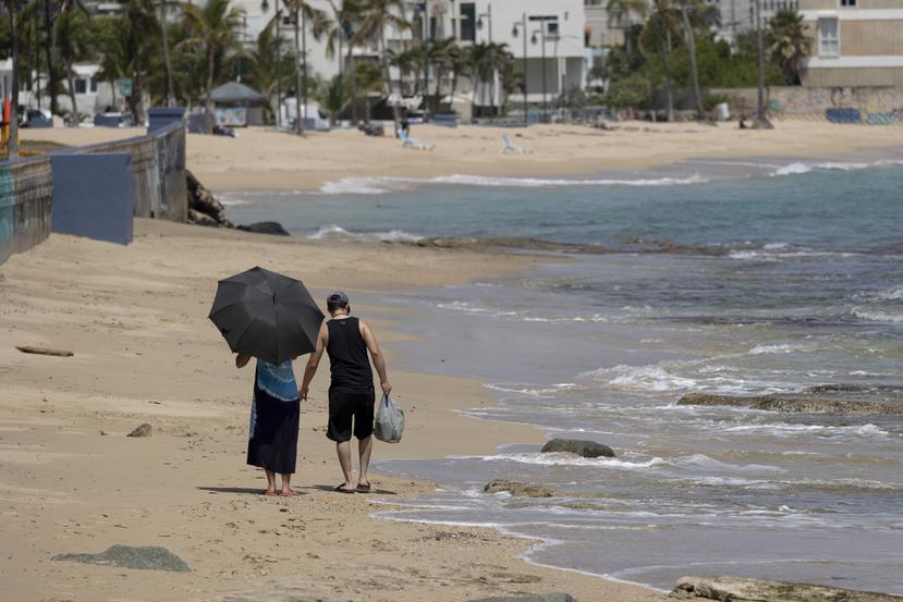Una mujer camina con una sombrilla por la playa durante un día en junio de 2023 en el que había aviso de calor extremo en San Juan.