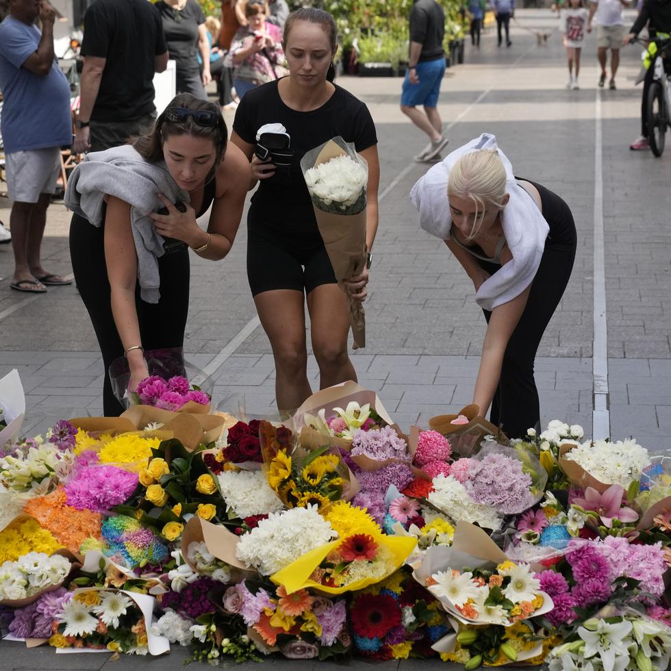 Tres mujeres colocan flores cerca del lugar en el cual se reportó el ataque, en un centro comercial en Sídney.