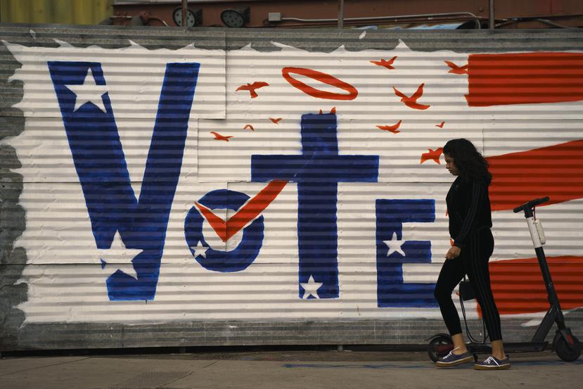 Una mujer camina frente a un letrero de votación pintado en una pared en un área de Venice Beach en Los Ángeles.