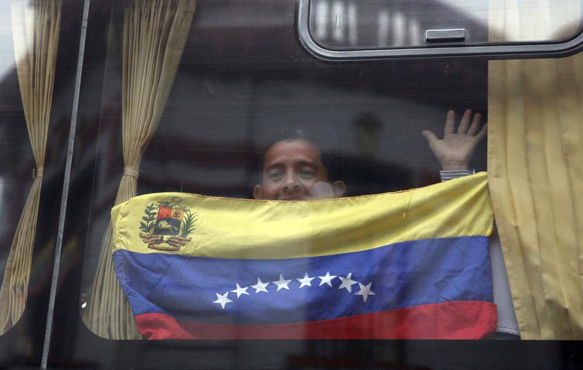 Un migrante venezolano con la bandera nacional saluda desde un bus que lo llevará al aeropuerto de Lima para el regreso a su país. (AP)