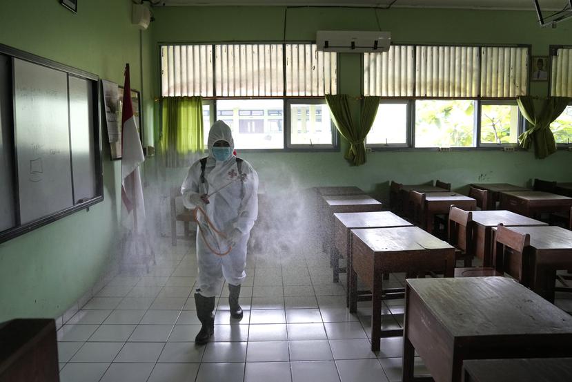 Un trabajador de LA Cruz Roja rocía desinfectante en un salón de clases vacío después de que se detectara un caso de COVID-19 en una escuela de Yakarta, Indonesia, el viernes 28 de enero de 2022.