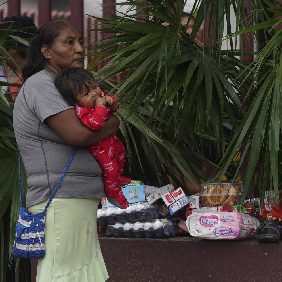 Una mujer sostiene a un bebé en brazos junto a varios objetos saqueados luego del huracán Otis.