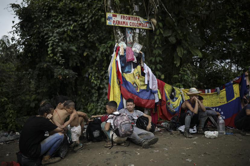 Migrantes sentados bajo un letrero que marca la frontera entre Panamá y Colombia durante su recorrido a través de la región del Darién, el martes 9 de mayo de 2023.