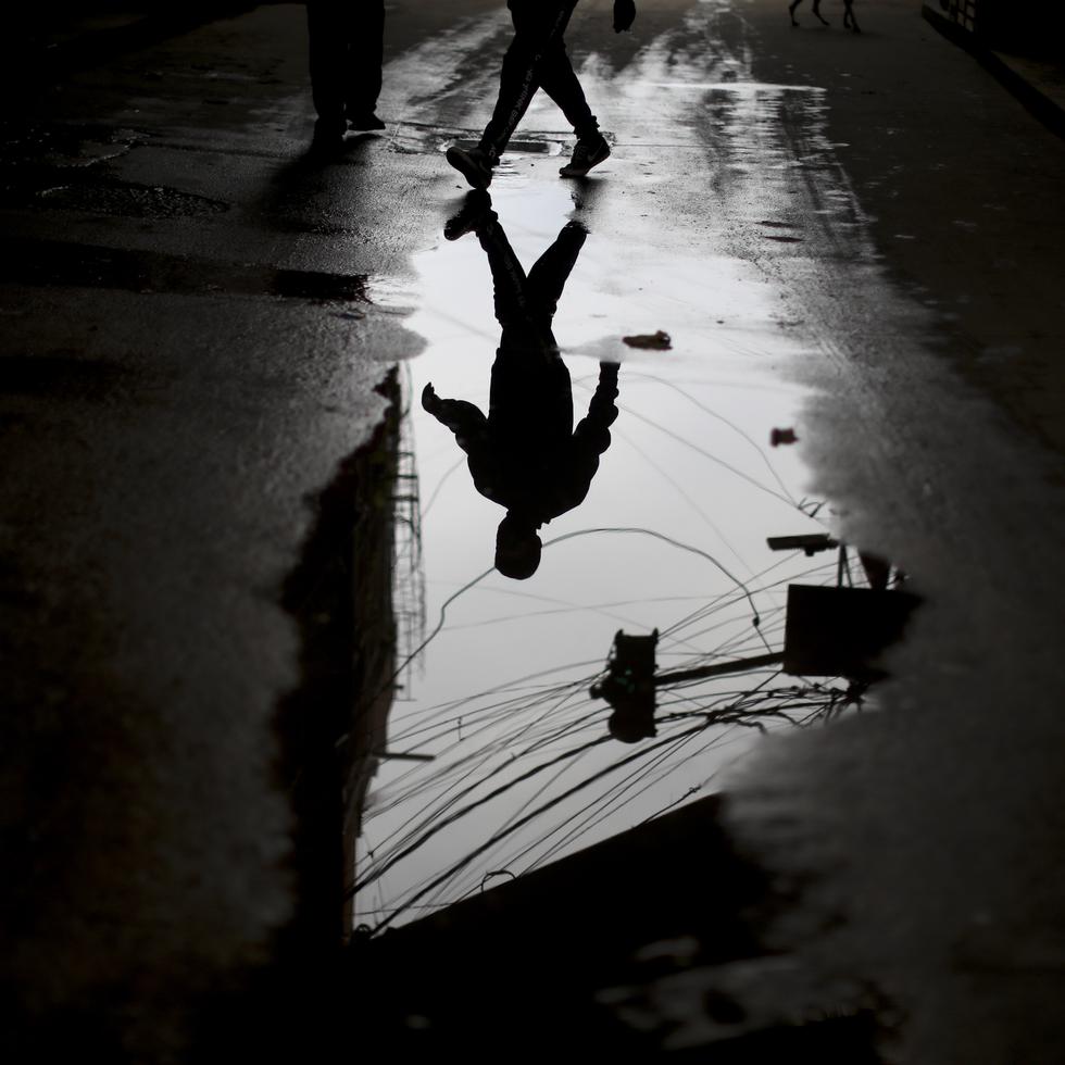 A pedestrian is reflected in a puddle in the “Villa 31” neighborhood during a government-ordered lockdown to curb the spread of the new coronavirus in Buenos Aires, Argentina, Tuesday, May 5, 2020. According to official data, the number of confirmed cases of COVID-19 disease in this city’s slum have increased in the past week, putting authorities on high alert. (AP Photo/Natacha Pisarenko)