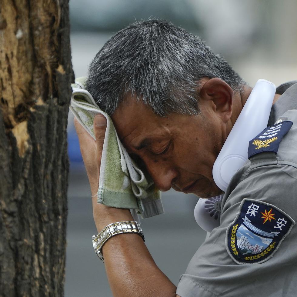 Un guardia de seguridad que lleva un ventilador eléctrico en el cuello se seca el sudor en un día caluroso en Beijing, el lunes 3 de julio de 2023.