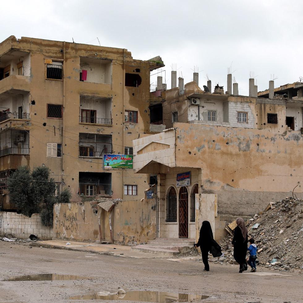 Dos mujeres sirias caminan junto a un niño frente a casas derruidas en Al Raqa (Siria), ciudad que fue la capital de facto de los yihadistas del grupo Estado Islámico.