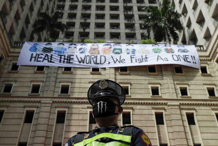 Un guardia de seguridad de pie ante una pancarta que dice "Sanen al mundo, luchamos como uno", en Filipinas. (AP)