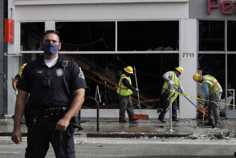Un oficial de policía se para frente a un edificio dañado por un incendio mientras trabajadores limpian los destrozos. (AP)