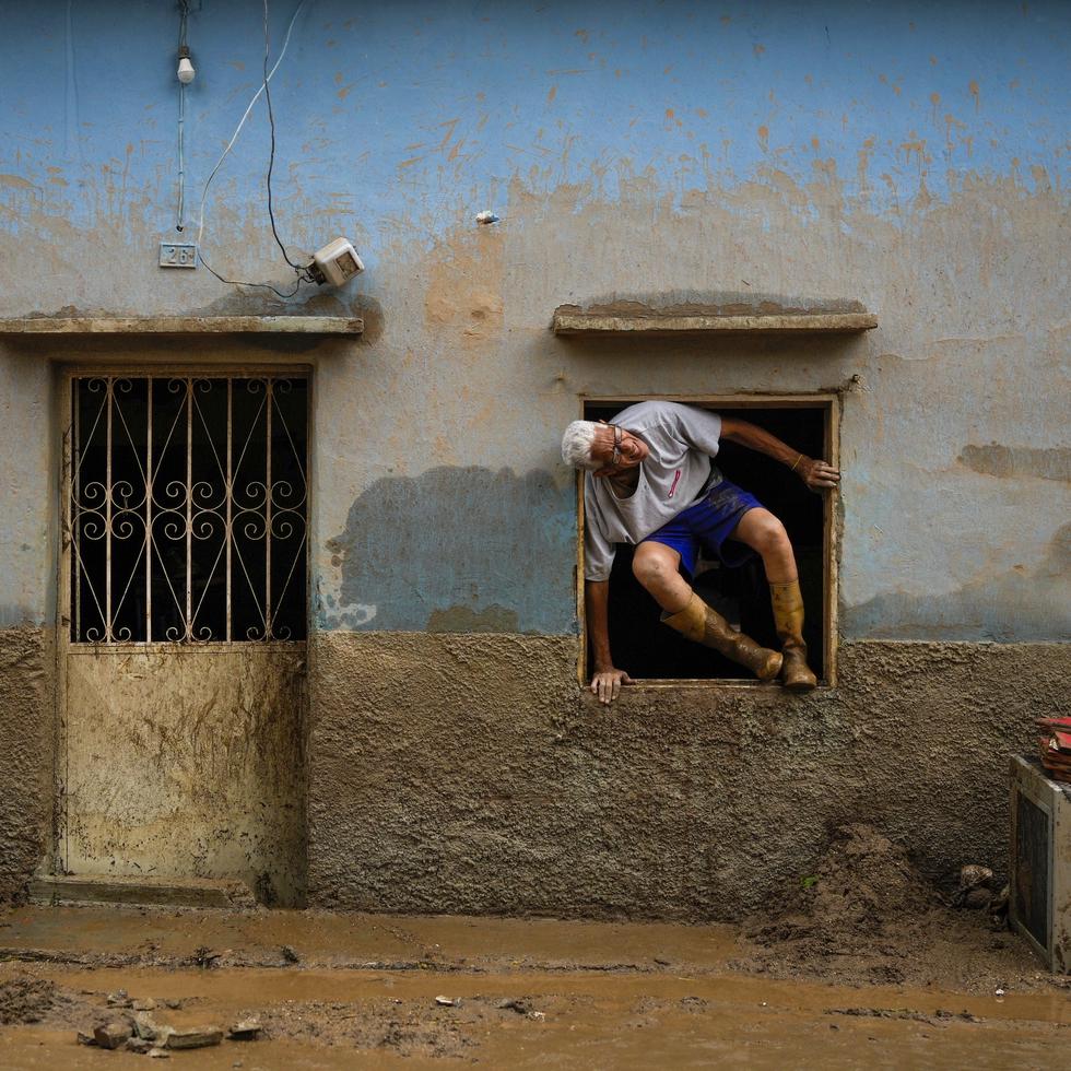 José Medina sale por la ventana de casa inundada por el desborde de un riachuelo a causa de las fuertes lluvias.