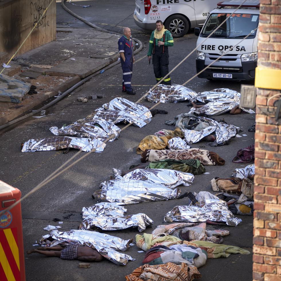 Varios médicos, junto a los cadáveres cubiertos de las víctimas de un incendio en un edificio del centro de Johannesburgo, el 31 de agosto de 2023.