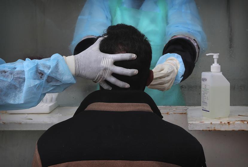 Un hombre es atendido por personal médico que le toma la muestra nasal para la prueba molecular de COVID-19 en India.