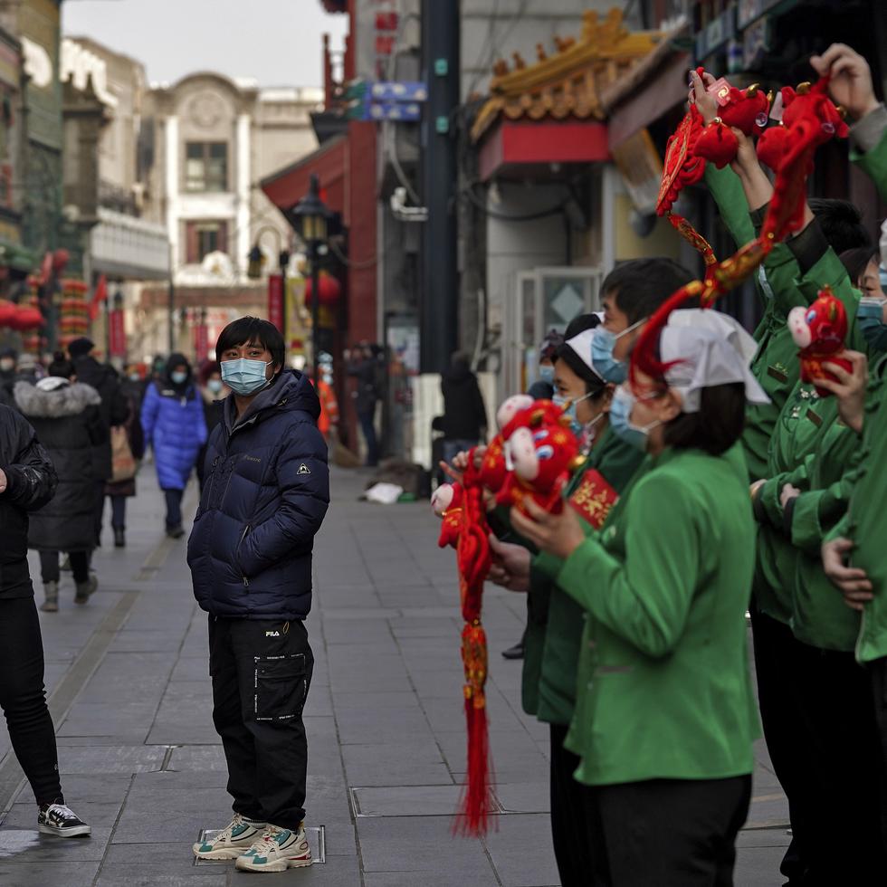 Unas personas con cubrebocas para protegerse del coronavirus cerca de la calle de comercios Qianmen, un sitio turístico en Beijing, China, el 31 de enero de 2021. (AP Foto/Andy Wong)