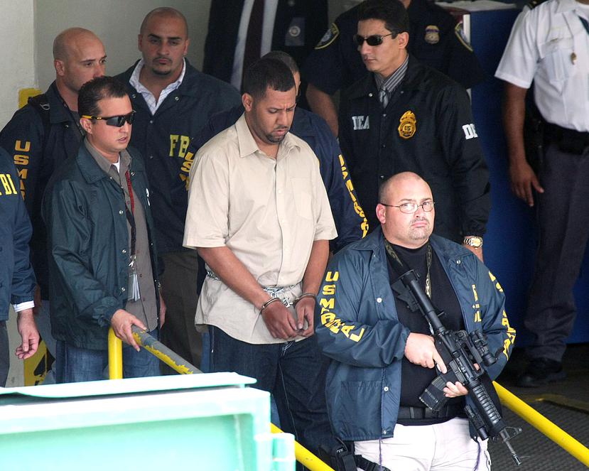 Foto de 2009 en la que se ve a Joseph González (atrás), actual director del FBI en Puerto Rico, que en aquel momento era el agente a cargo de la investigación contra Ángel Ayala Vázquez, mejor conocido como Ángelo Millones (al centro, esposado).