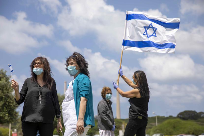 Personal médico y pacientes, todas con cubrebocas, alzan banderas israelíes mientras aviones de la fuerza aérea vuelan en formación sobre el centro médico Hillel Yaffe en el Día de la Independencia israelí. (AP)