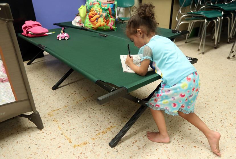 Una niña escribe en una libreta sobre uno de los catres que se colocan en los refugios. (GFR Media)