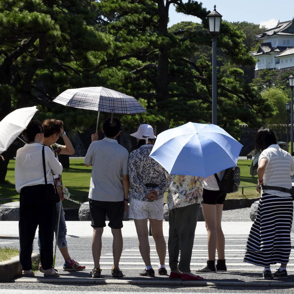 Varias personas se protegen del sol mientras pasean por los jardines del Palacio Imperial en Tokio, Japón.