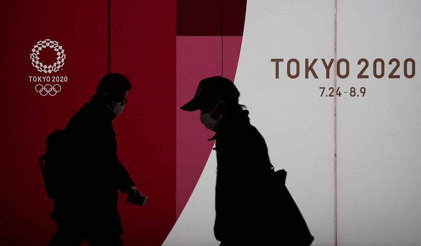 Peatones con máscaras caminan junto al emblema de los Juegos Olímpicos en Tokio hoy, lunes. (EFE)