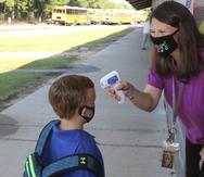 In a photo provided by Newton County Schools, teaching assistant Crystal May talks to kindergarten student Lewis Henry Thompson, 5, as she takes his temperature at Newton County Elementary School in Decatur, Miss., Monday, Aug. 3, 2020. Thousands of students across the nation resumed in-person school Monday for the first time since March. Parents are having to balance the children's need for socialization and instruction that school provides, with the reality that the U.S. death toll from the coronavirus has hit about 155,000 and cases are rising in numerous places.