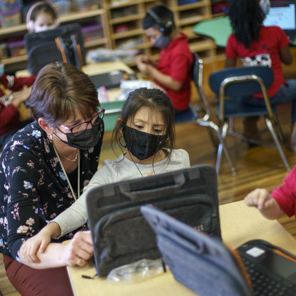 Kindergarten teacher Karen Drolet, left, works with a student at Raices Dual Language Academy, a public school in Central Falls, R.I., Wednesday, Feb. 9, 2022. As some of the last statewide mask mandates in the U.S. near an end, decisions about whether students and teachers should continue to wear masks in school are shifting to local leaders, who are caught in the middle of one of the most combustible issues of the pandemic. (AP Photo/David Goldman)