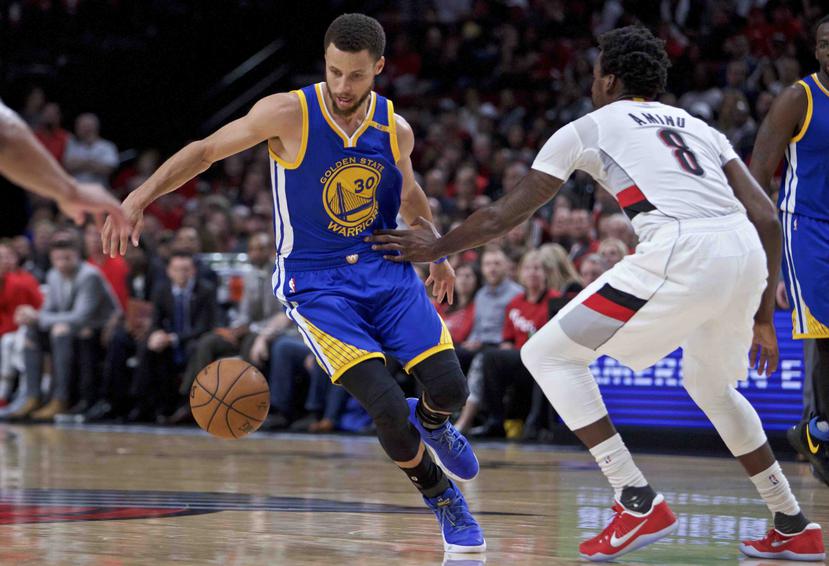 El jugador de los Warriors de Golden State Stephen Curry, a la izquierda, bota a su espalda para eludir al jugador de los Trail Blazers de Portland Al-Farouq Aminu. (AP)