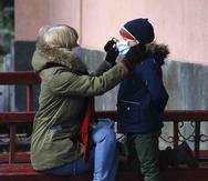 Una madre le coloca una mascarilla protectora a su hijo en Ucrania. (AP)