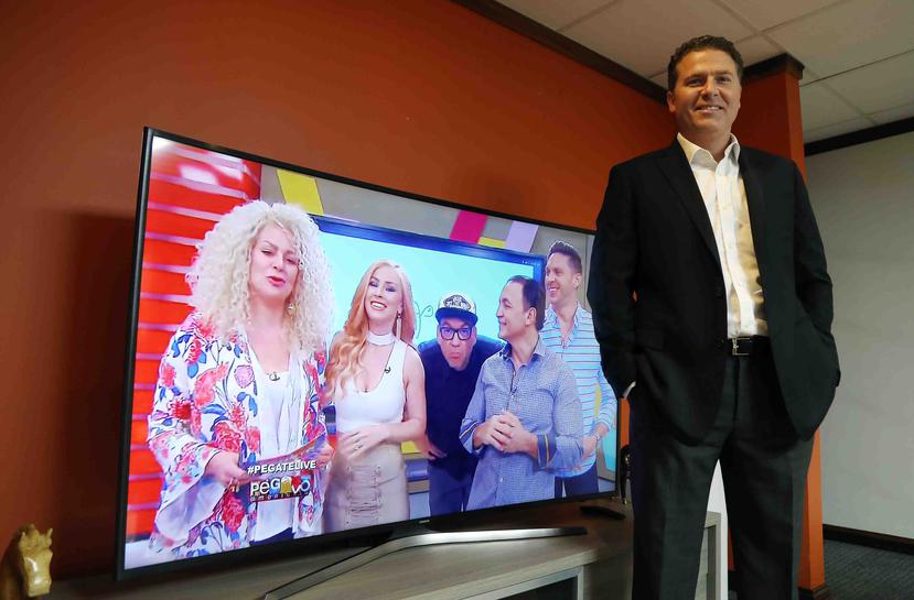 Javier Maynulet posa al lado de un televisor en el que se observa el programa "Pégate al Mediodía".