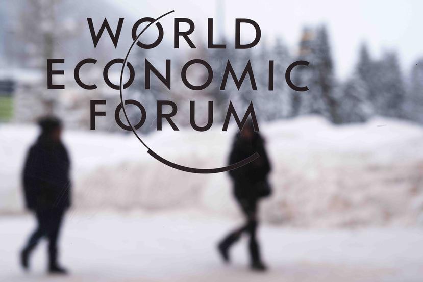 Dos personas caminan por detrás del logo del Foro Económico Mundial. (AP)