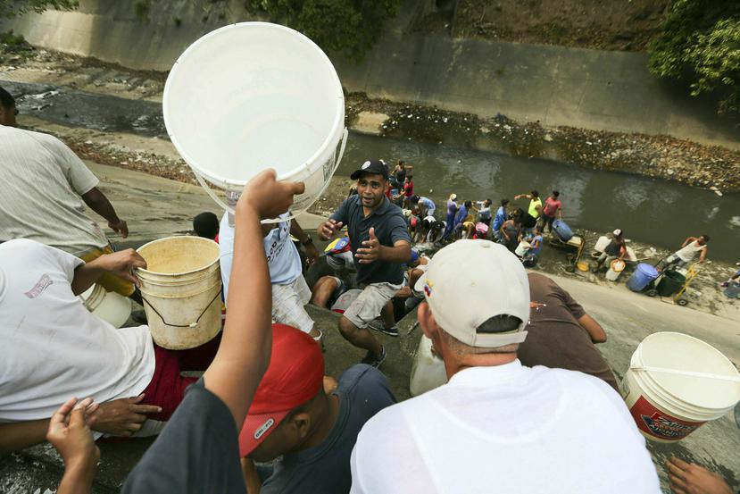 Tras el apagón, muchos venezolanos han salido a recoger agua de una tubería que gotea sobre el río Guaire, ya que los apagones afectaron las bombas de agua en las casas, oficinas y tiendas de Caracas. (AP Foto/Fernando Llano)