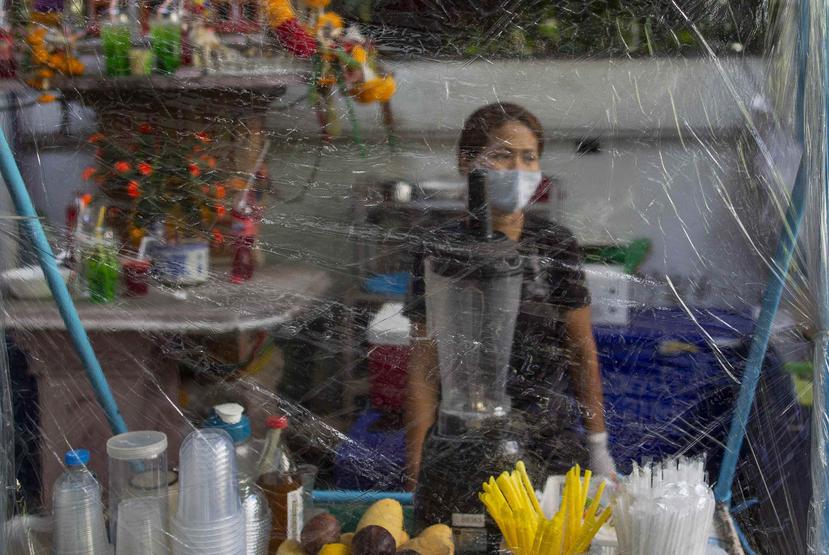 Una vendedora callejera espera detrás de un plástico, en Bangkok, Tailandia. (AP)