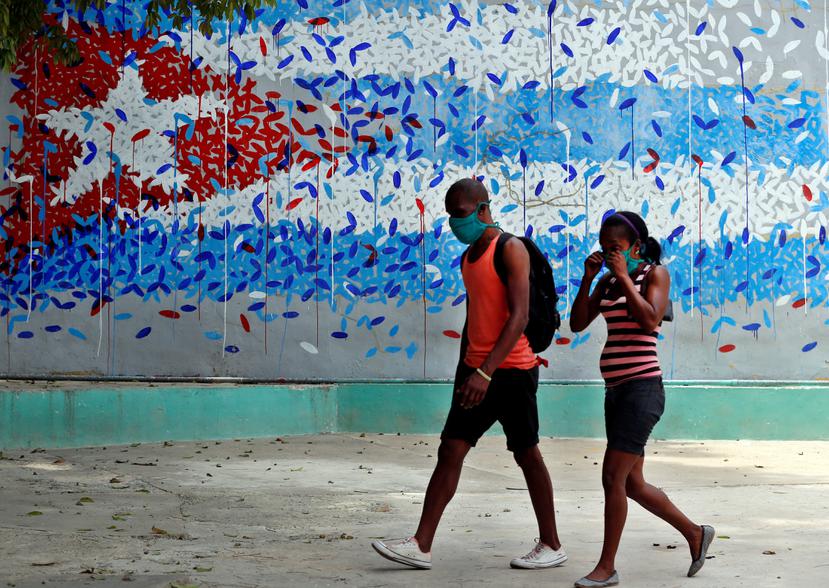 Una pareja con tapabocas camina junto a un graffitis con la imagen de la bandera cubana, en La Habana (Cuba).