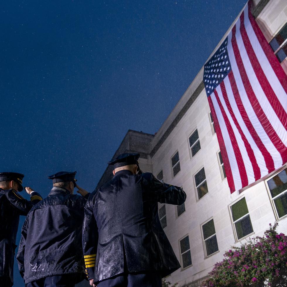 Socorristas saludan bajo una lluvia torrencial mientras se despliega una bandera de Estados Unidos en el Pentágono en Washington, al amanecer del 21 aniversario de los ataques terroristas del 11 de septiembre.