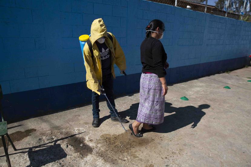 Un trabajador con equipo de protección rocía un desinfectante en la parte inferior de los zapatos de una mujer como precaución contra la propagación del nuevo coronavirus antes de ingresar a la escuela de su hijo. (AP)