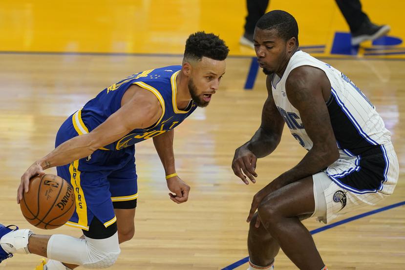 El jugador de los Warriors de Golden State Stephen Curry (izquierda) intenta esquivar a su rival del Magic de Orlando Gary Clark durante la primera mitad del juego de la NBA que enfrentó a ambos equipos en San Francisco, el 11 de febrero de 2021.