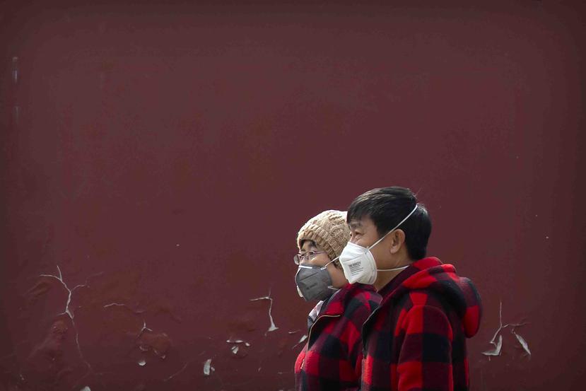 Dos personas con mascarillas sobre la boca pasan por un parque público en Beijing. (AP)