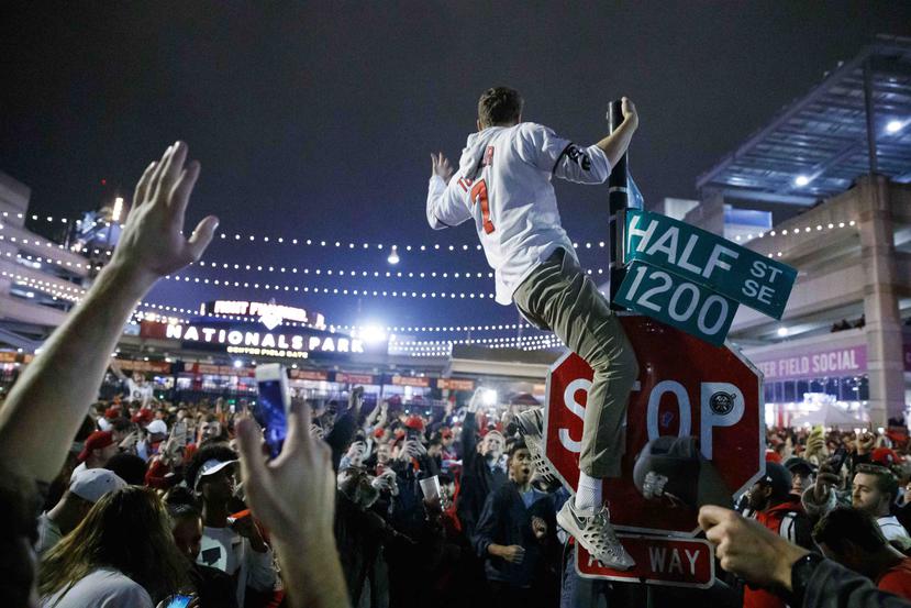 Un aficionado de los Nationals escala un poste a las afueras de Nationals Park a primeras horas después de que el equipo derrotara a los Astros de Houston en el séptimo juego de la Serie Mundial. (AP/Alex Brandon)