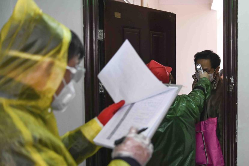 En esta imagen del 18 de febrero de 2020 publicada por la agencia de noticias Xinhua, trabajadores van puerta a puerta para comprobar la temperatura corporal de los vecinos durante una campaña de control de enfermedades en el vecindario de Qingheju, distr