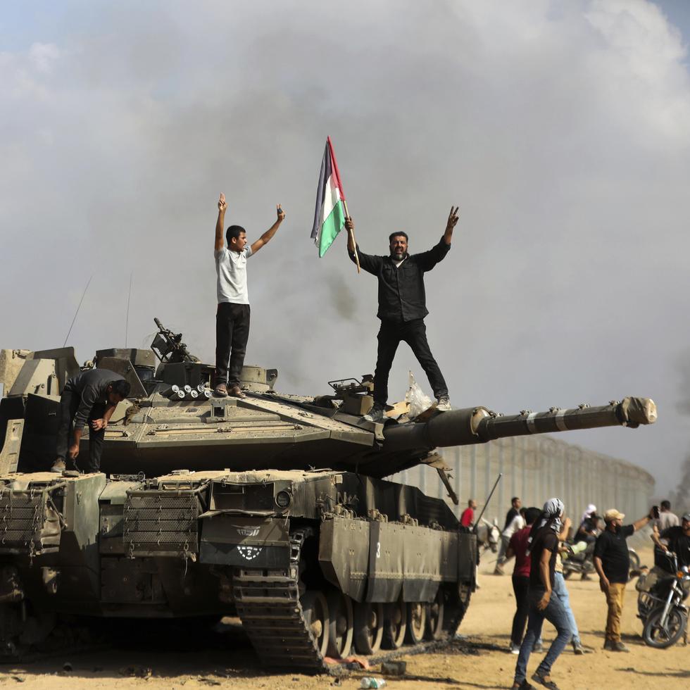 Palestinos ondean una bandera nacional y celebran junto a un tanque israelí destruido en la valla fronteriza que separa la Franja de Gaza de Israel.
