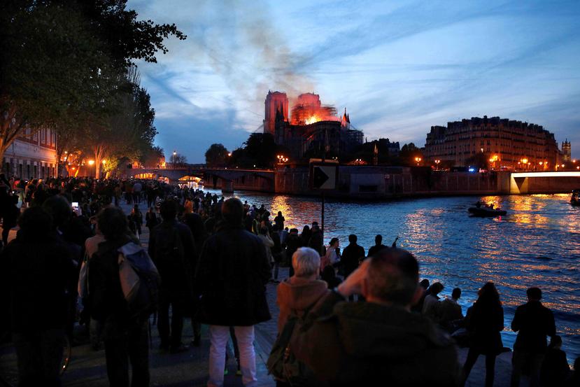 Decenas de personas en la orilla del río Sena observan la columna de humo y las llamas que consumen a la catedral de Notre Dame este lunes, en París.  (EFE)