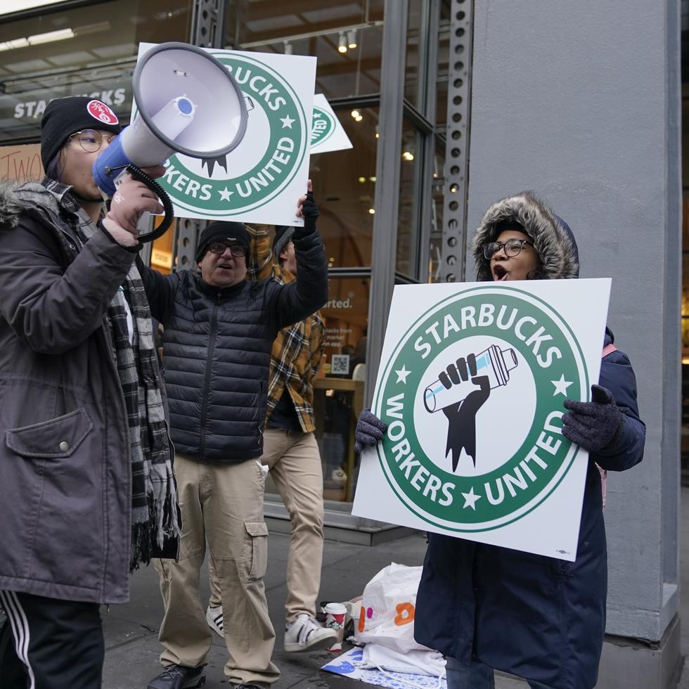 Personas alzan carteles frente a un local de Starbucks en Nueva York, jueves 17 de noviembre de 2022, en reclamo de aumentos salariales y otros beneficios.