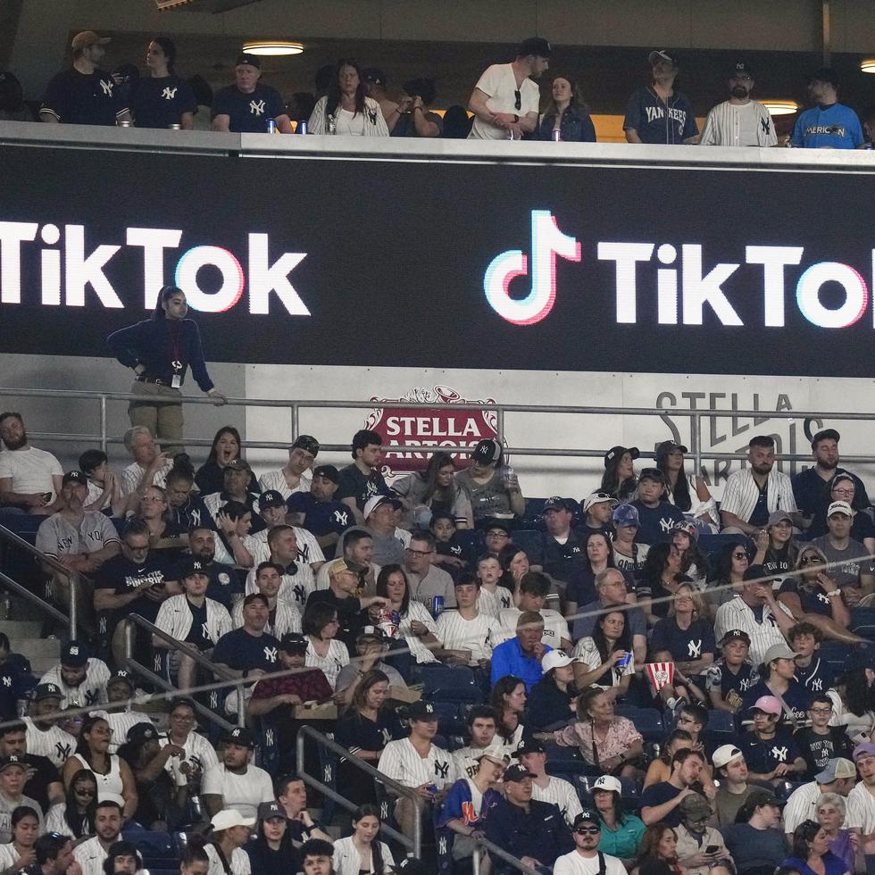 Aficionados están sentados bajo un anuncio de TikTok mientras asisten a un partido de béisbol en el Yankee Stadium.