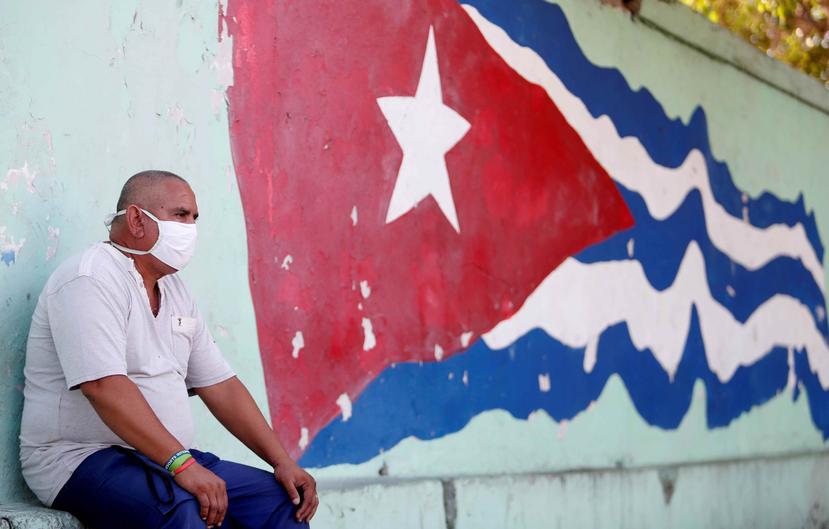 Un hombre sentado al lado de una bandera cubana pintada en un muro en La Habana. (AP)