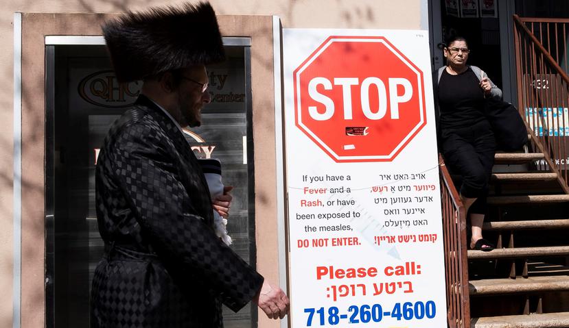 Un hombre camina junto a un cartel que alerta contra el sarampión en Brooklyn, Nueva York. (Agencia EFE)