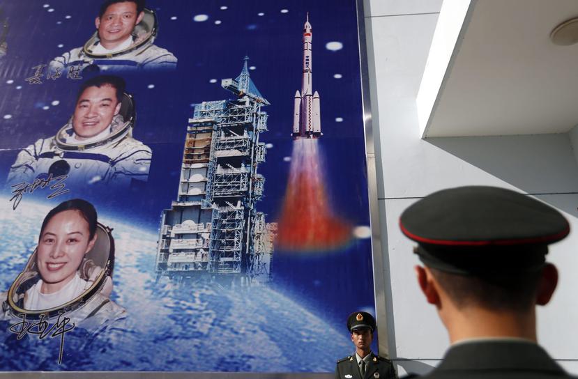 Militares chinos hacen guardia frente a un letrero que muestra la foto de varios astronautas y el lanzamiento de un cohete. (EFE)